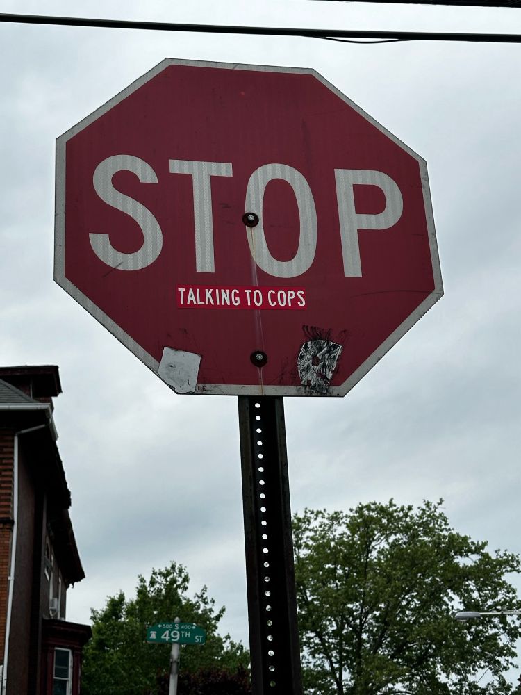 Stop sign with a sticker below the letters STOP that says “Talking to Cops”.