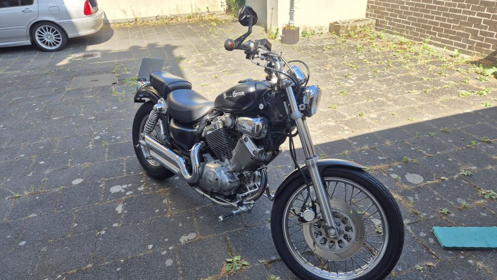 Schwarzes Custom Bike mit V-Motor, glänzenden Chromdetails und dem Schriftzug ‚Black Edition‘ auf dem Tank, basierend auf einer alten Yamaha Virago, geparkt auf einem gepflasterten Hof.
