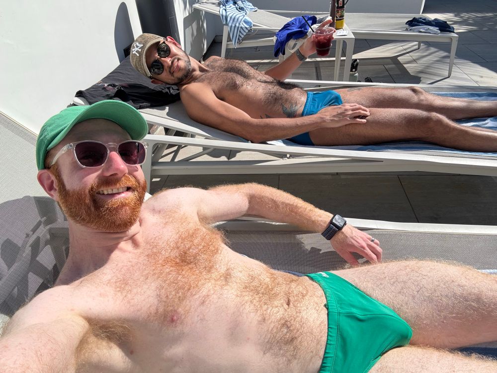 Two hairy men on pool chairs wearing Speedos lounging in the sun. 