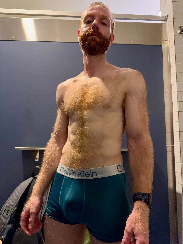 Hair toned ginger man standing in change room wearing blue Calvin Klein trunks 
