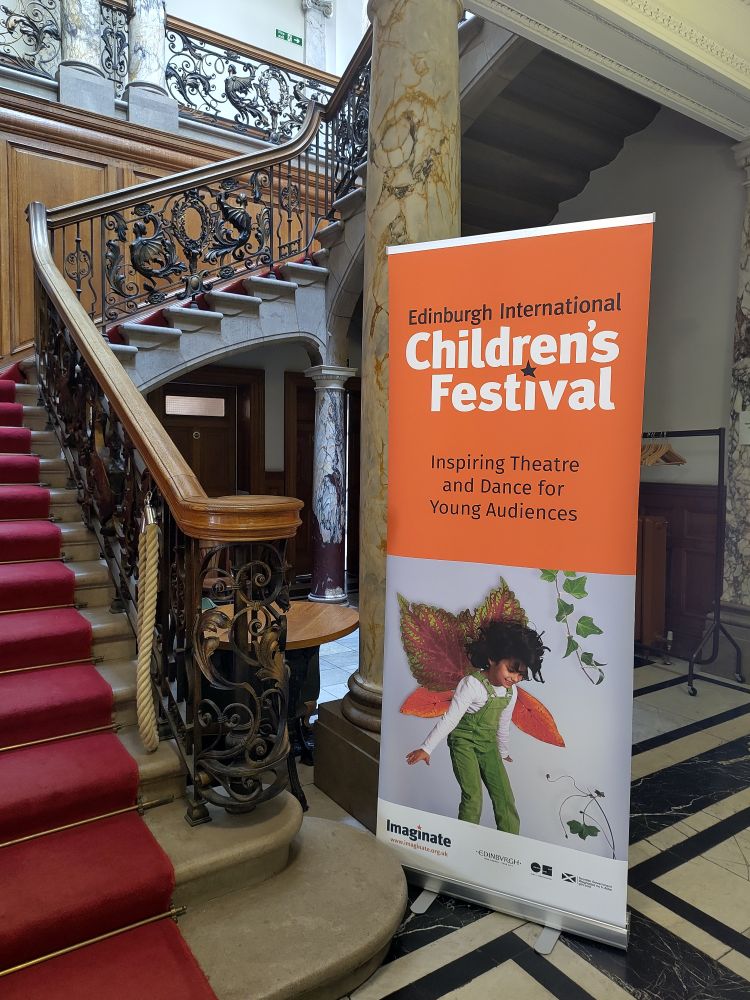 A banner advertising the Edinburgh International Children's Festival at the base of a curved staircase 