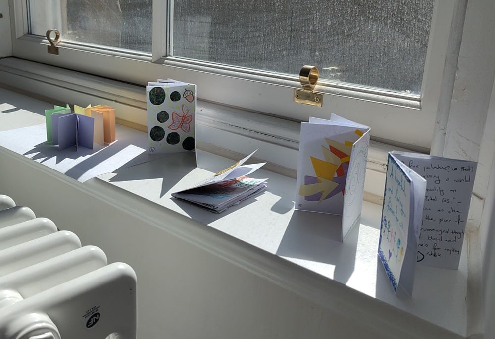 Sunny windowsill with 4 mini zines resting on it, and to the left, pastel coloured blank tiny versions of zine/books