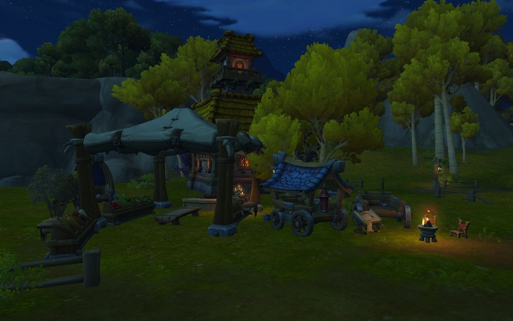 The backyard of a house in World of Warcraft (the same home as the previous image) that has a small farmer's market set up under a large white tent. There are covered and uncovered wagons sitting to the sides and a small fire with chairs around it by the wagons. In the distance you can see golden leaved trees.