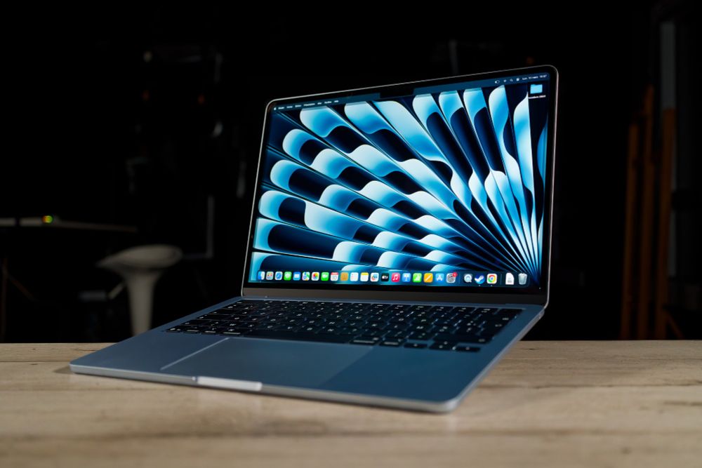 Photo du Macbook air m4 en colori bleu ciel sur une table en bois et un fond sombre.