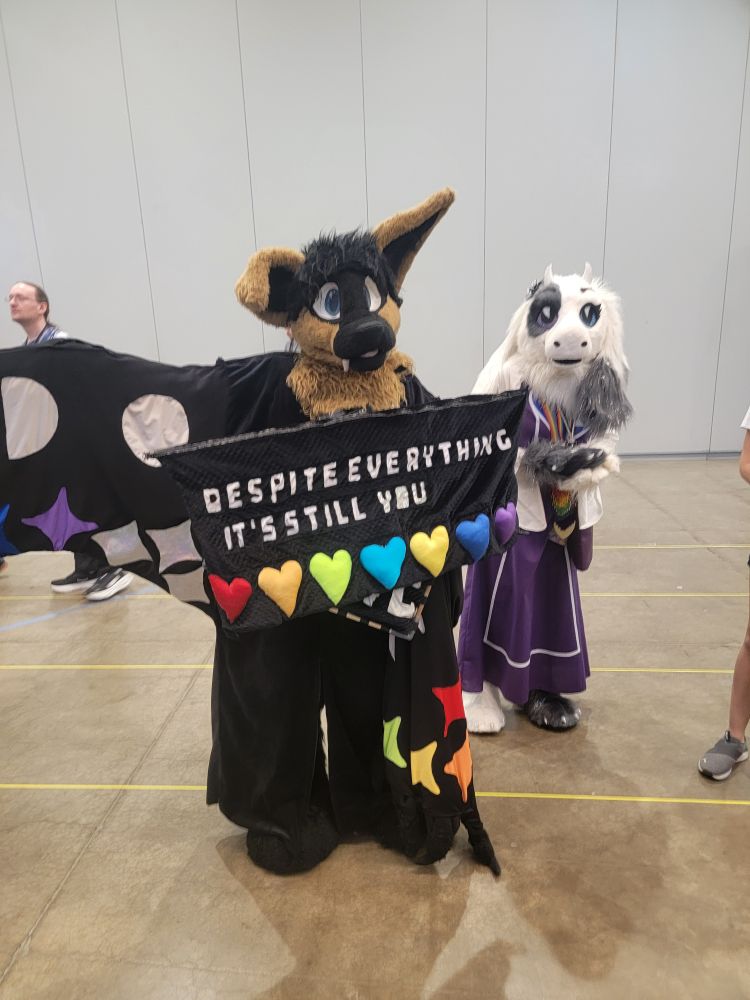 Mangofruitbat at the Undertale/Deltarune meet up at Anthrocon 2025, displaying a sign that says, "Despite everything,  it's still you."