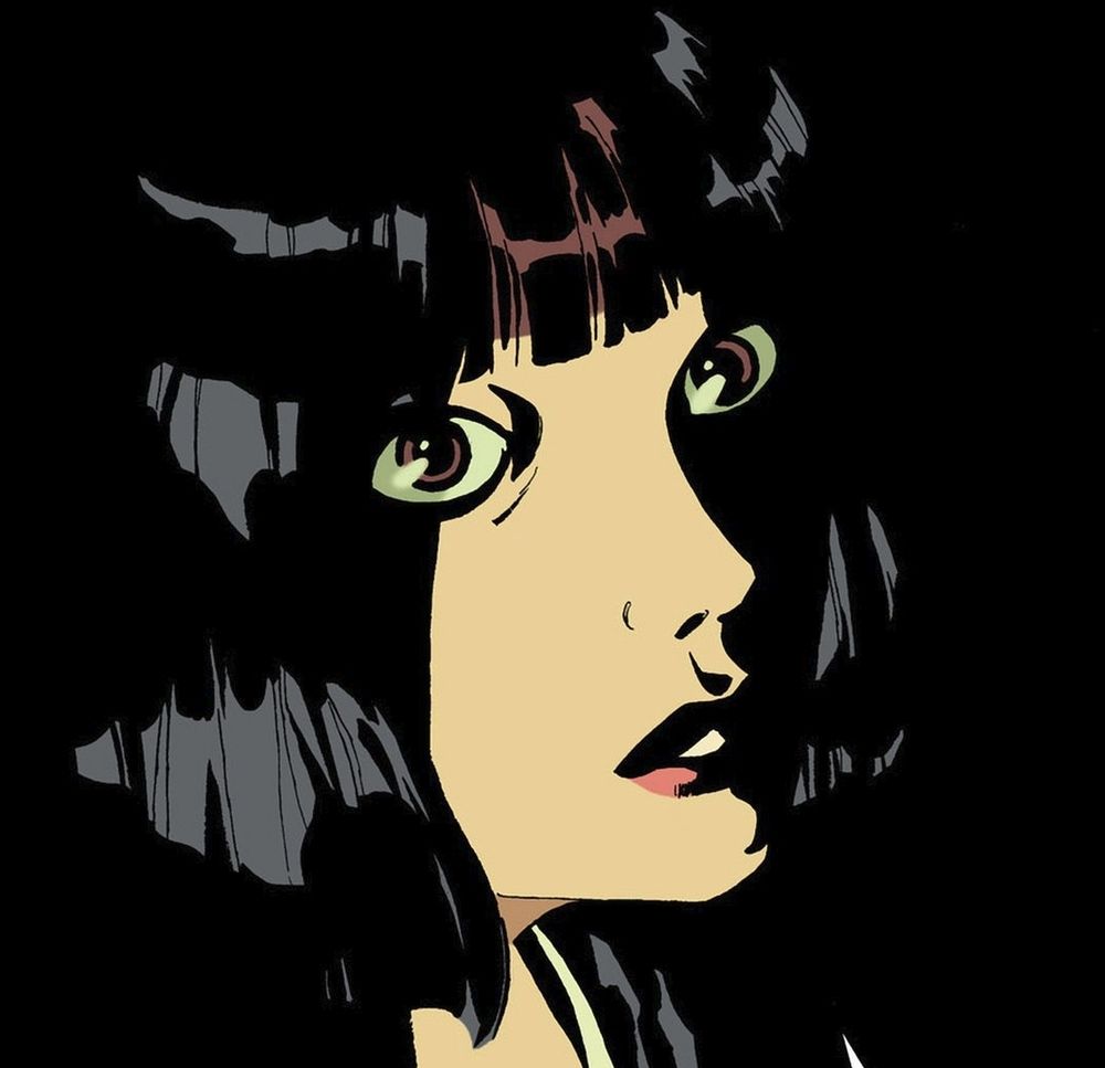 rosto de uma mulher branca de cabelos pretos curtos, em um ambiente todo preto