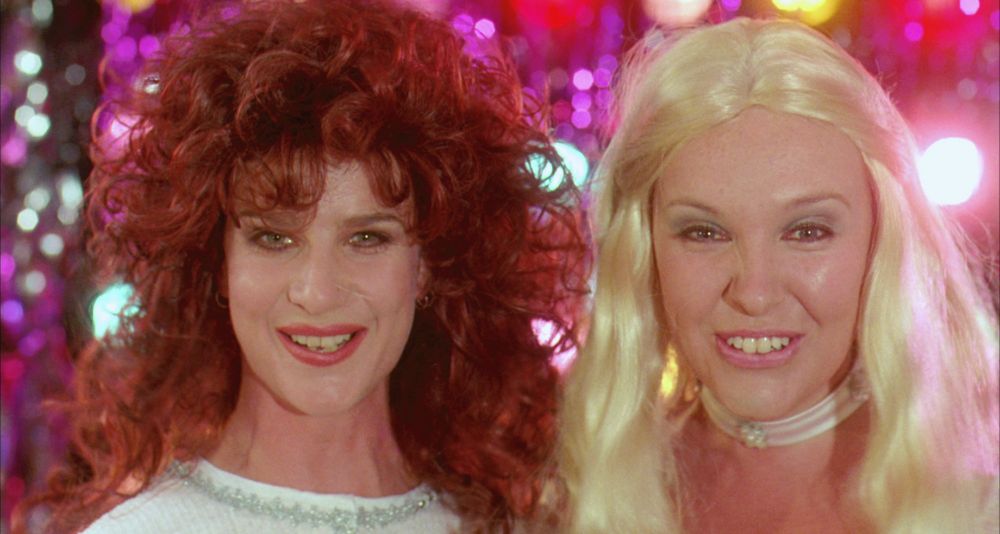Image from Muriel's Wedding with the two main characters wearing wigs and smiling at the camera