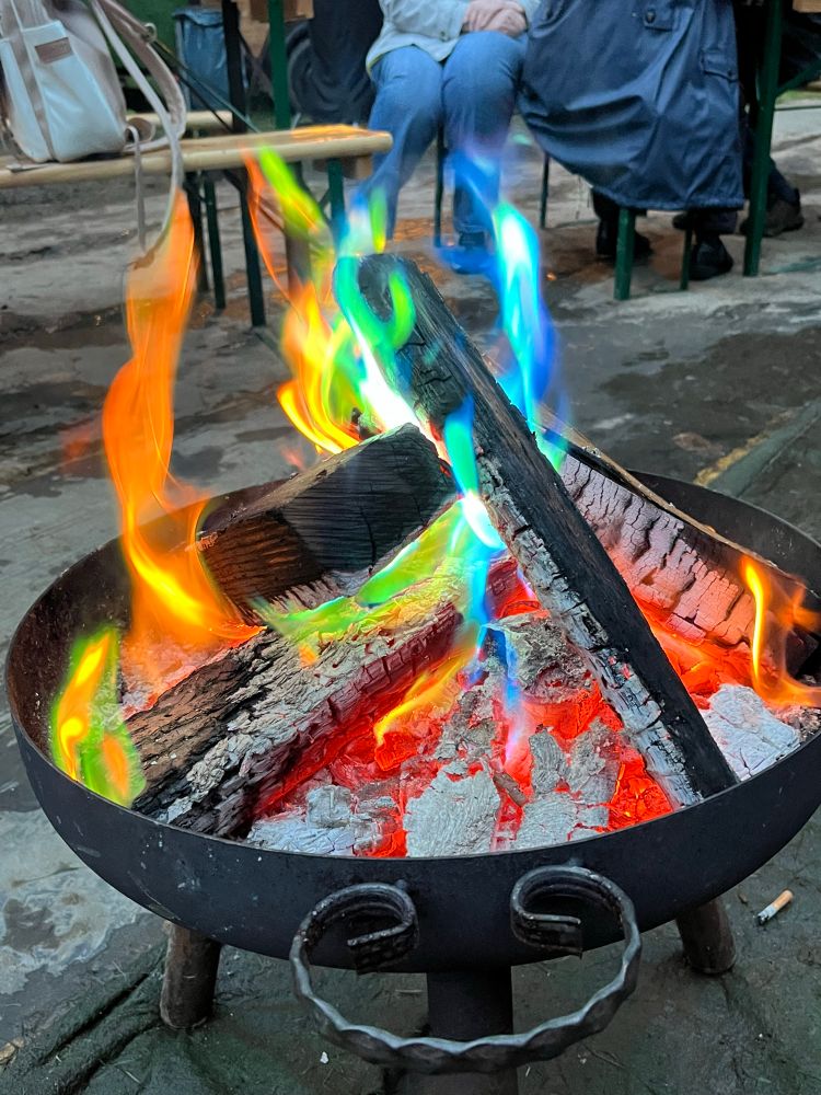 Eine Feuerschale mit brennenden Holzscheite, diese brennen in bunten Farben.