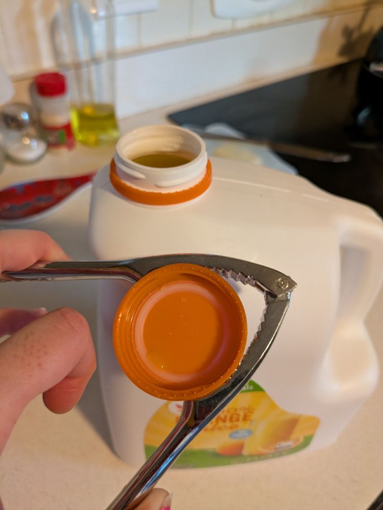 Opened bottle of orange juice, nutcracker holding the cap, no hand streny