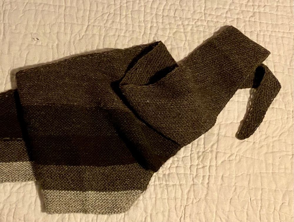 A long triangular shawl striped in shades of brown and gray, loosely folded upon itself. 