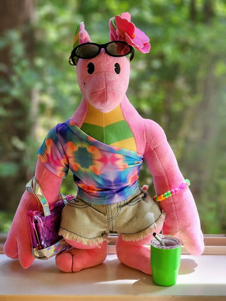 The Gummy Plush dressed up with denim shorts, a colorful off-shoulder shirt, beach bag with towel, sunglasses, and a flower on their ear! Most clothing from Build-a-Bear