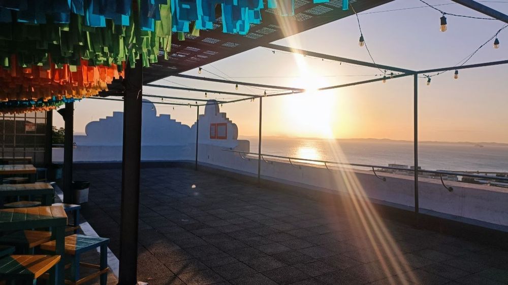 Foto da vista do restaurante, que rica num terraço. Dá pra ver o sol se pondo no mar.