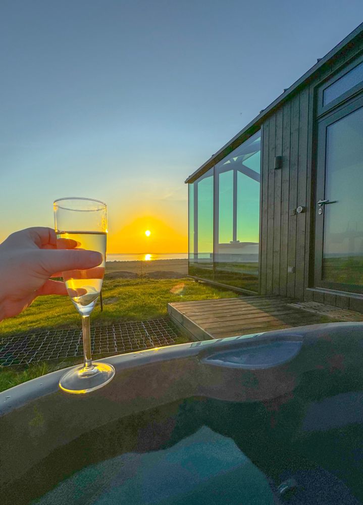 Champaign cheers to the midnight sun in a hot tub next to a glass house and the Icelandic coast 