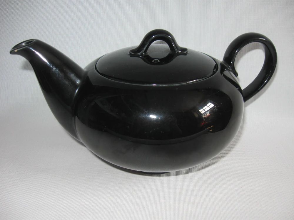 Homer Laughlin Charm House teapot in shiny black. Made in the 50s, with a very MCM mid century modern look!  The body is a somewhat flattened ball shape, with the lid completing the round of the body.  Spout originates from the bottom of the pot and swoops up in a generous arc to form a rather small diagonal opening compared to the wideness of where it's attached to the pot.  Handle is a generous, upward tilting C-shape.  Lid has a simple arc-shaped handle with little side-tabs, and a vent hole.  These pots are seldom marked, for some weird reason. 