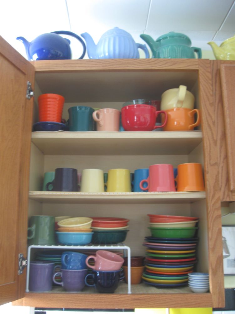 A kitchen cabinet full of mostly newer Homer Laughlin Fiesta dishes, with a few vintage items here and there. Also, a small stack of Oven Serve dishes, and some little Chinese "prep" dishes, and a "new" Bauer orange ringware tumbler. 