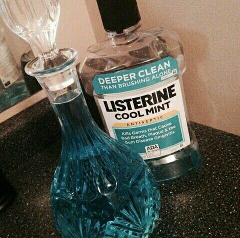 garrafa de listerine cool mint vazia do lado de uma garrafa de vidro com tampa tbm de vidro cheia com o listerine (a cor do liquido é turquesa, clássico do listerine), a garrafa tem detalhes e texturas, o formato da garrafa é classico de poção de ficção, a aparte de baixo bem redonda e a tampa é uma bolinha 