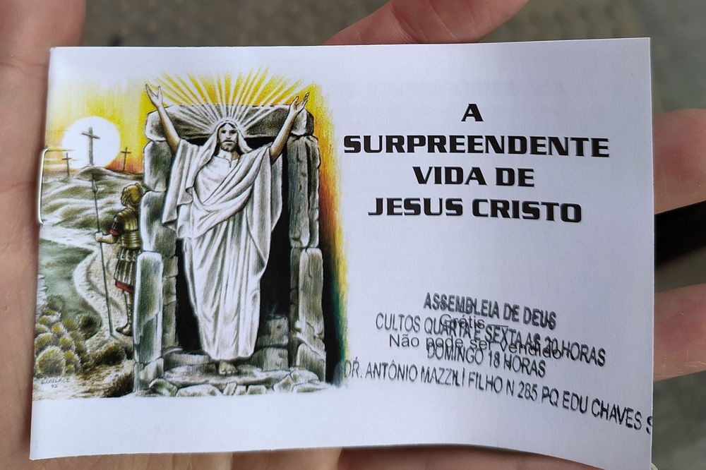 Livrinho menor que minha palma da mão com um desenho colorido de jesus de corpo inteiro, comemorando com os braços pra cima  saindo de uma Dungeon, ele tem brilho na cabeça, ele deve ter pego um artefato raro, do lado dessa imagem está o título da aventura: a surpreendente vida de jesus cristo, em baixo está carimbado assembleia de deus e outras informações que foram carimbado mais de uma vez e dificulta a leitura