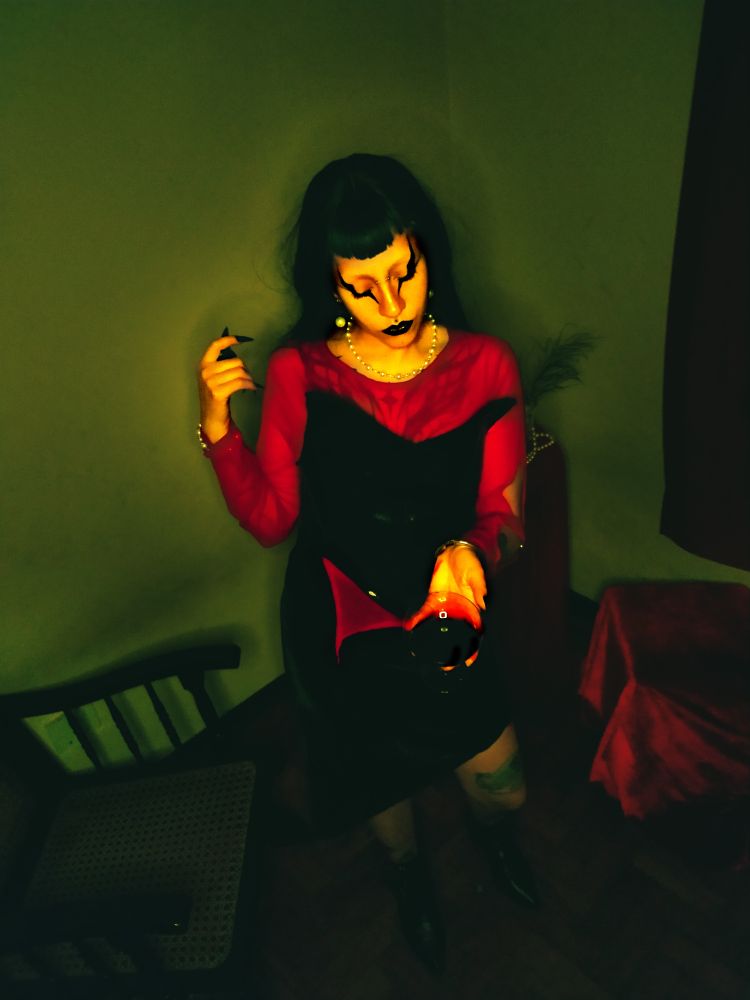 a mesma garota com o mesmo look da foto passada, porem nessa pose ela esta segurando uma taça de "sangue" como se estivesse te oferecendo, nessa foto o filtro não é mais quente e sim esverdeado meio jogo de terror do ps2 