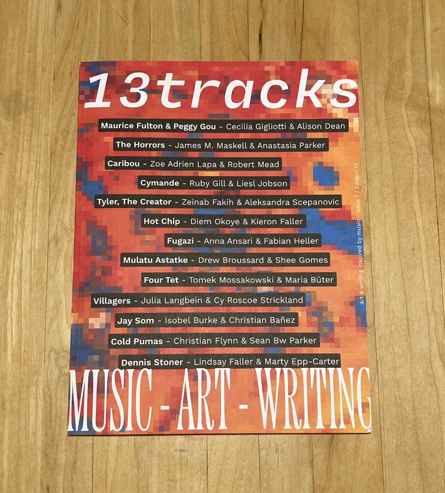 The first issue of 13Tracks Magazine sits square on a wooden table. The magazine is densely designed, with 13tracks on top in an italic font, with 13 black bars staggered below, each with a musician/band’s name in bold followed by the names of two respondents. At the bottom, MUSIC - ART - WRITING.
The backdrop is a glitchy orange/blue/red illustration.