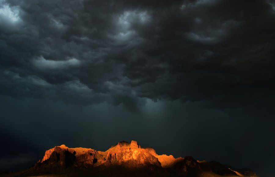 Sunset light illuminating Superstition Mountain underneath a brooding, ominous, roiling cloudscape. 