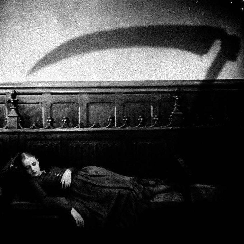 Black and white film still of a woman and a black dress asleep on a bench on the wall above her is the shadow of a Scythe 
