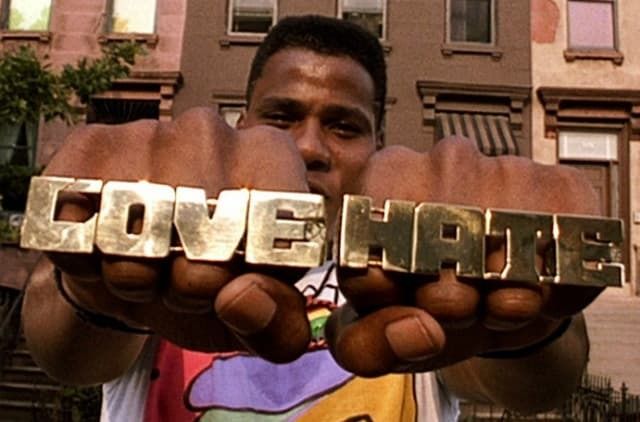 A film still of Radio Raheem showing off his knuckle rings -- across all four of his knuckles are big gold letters spelling out LOVE and HATE
