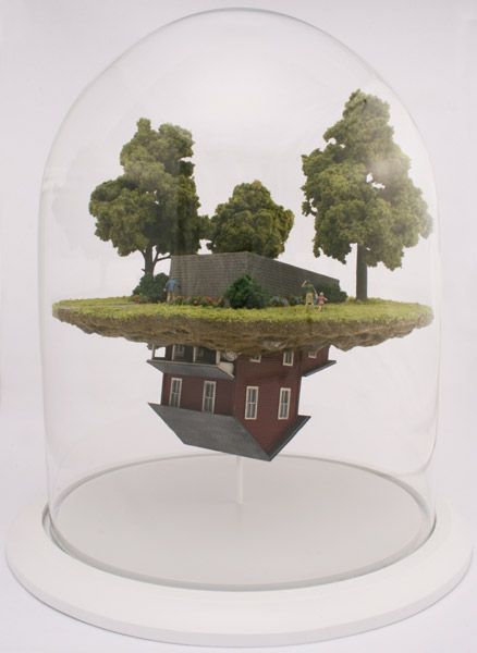 Under a glass dome there is a little diorama - a green lawn with a few trees and a family of three walking around. In the middle of this are the foundations of a house. But the foundations are upside down. below the disc of green lawn which holds the scene on top is another scene where the house has penetrated the green and is hanging upside down.