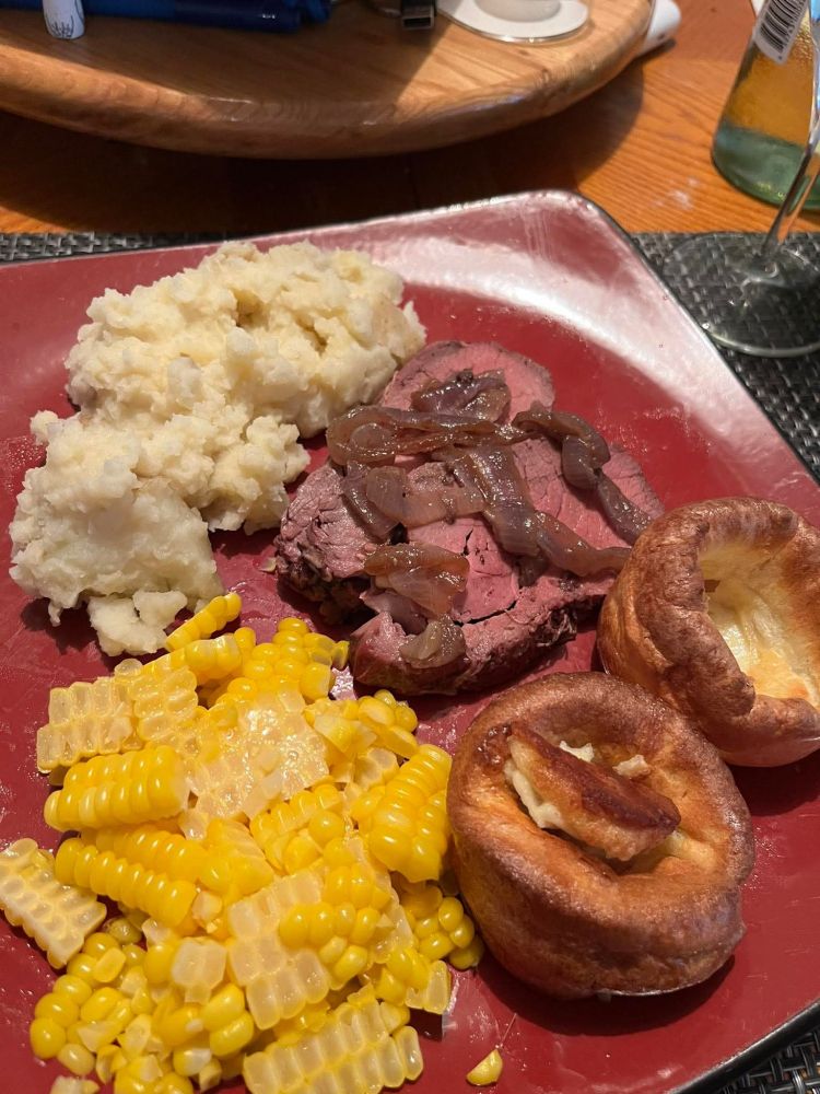 Dinner plate with mashed potatoes, corn, Yorkshire Puddings, roast tenderloin with onions and gravy.