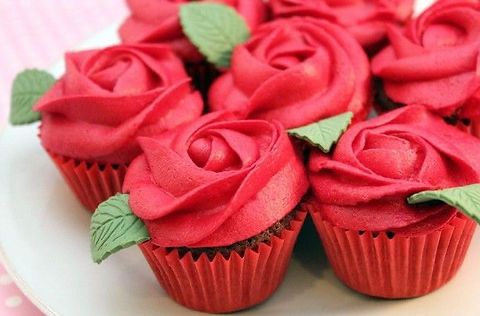 Cupcakes covered in red roses made from butter cream icing with small edible green pedals