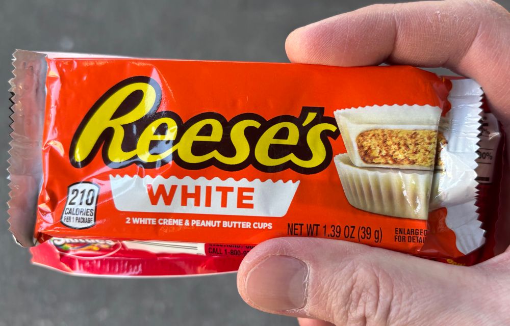 Two Reese’s peanut butter cups in their distinctive orange packaging but with white chocolate instead of the traditional brown.