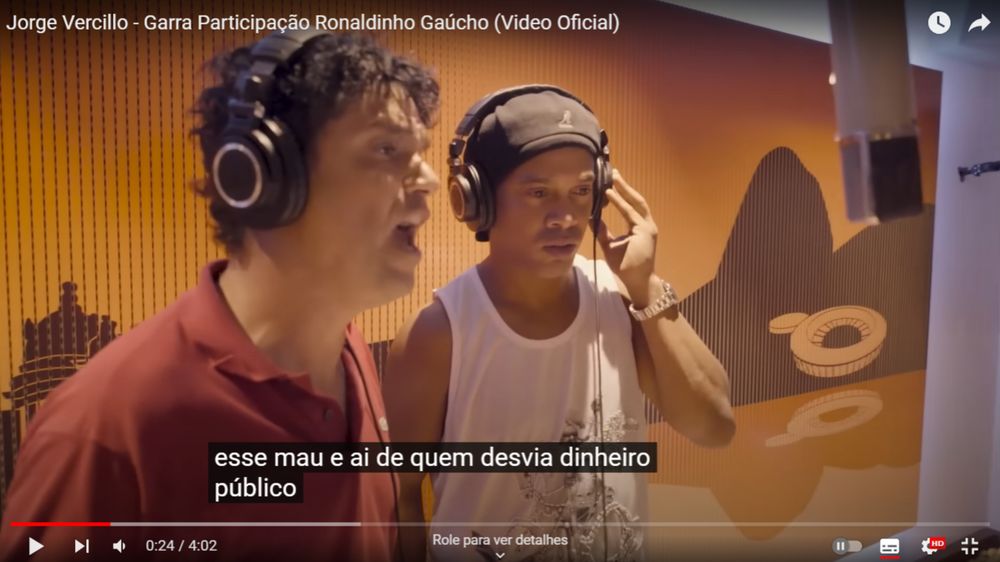print do clipe de Garra, do Jorge Vercillo com participação do Ronaldinho Gaúcho, no youtube, em que se vê os dois na tela com a legenda "esse mau e ai de quem desvia dinheiro público"