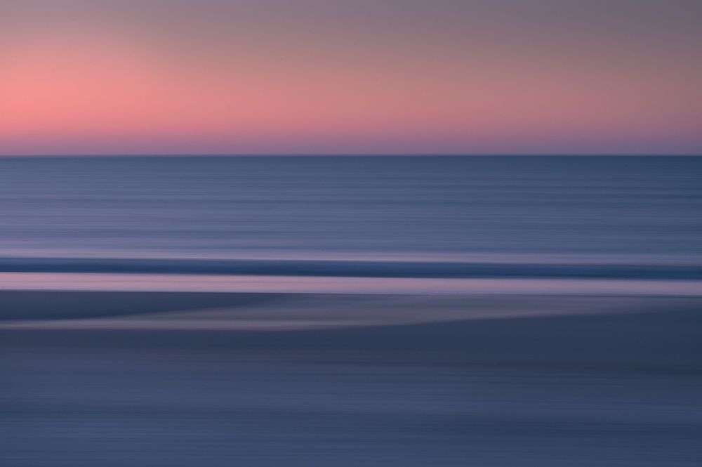 ICM image of the beach at sunrise. Pinks, blues, glowing silver, image is horizontally linear, yet conjures up the feeling of movement.