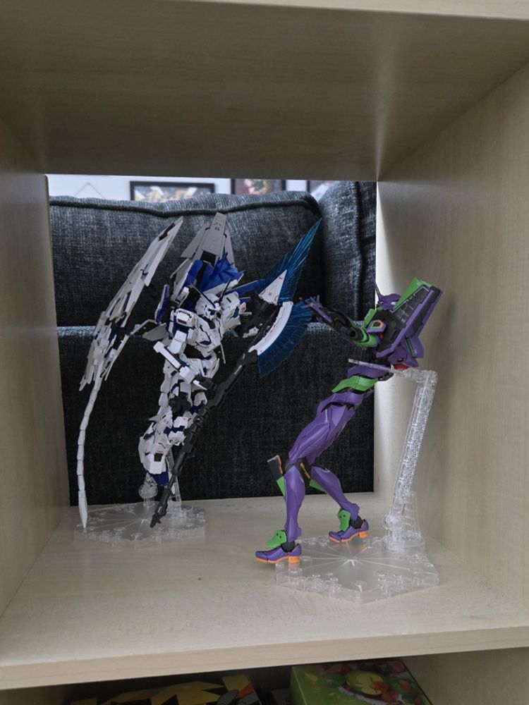 RG Gundam Unicorn Perfectibility posed with its axe attacking the RG Evangelion Unit 01. The Unicorn is flying forward with axe in front while Unit 01 is leaned back defending the atrack with a prog knife.