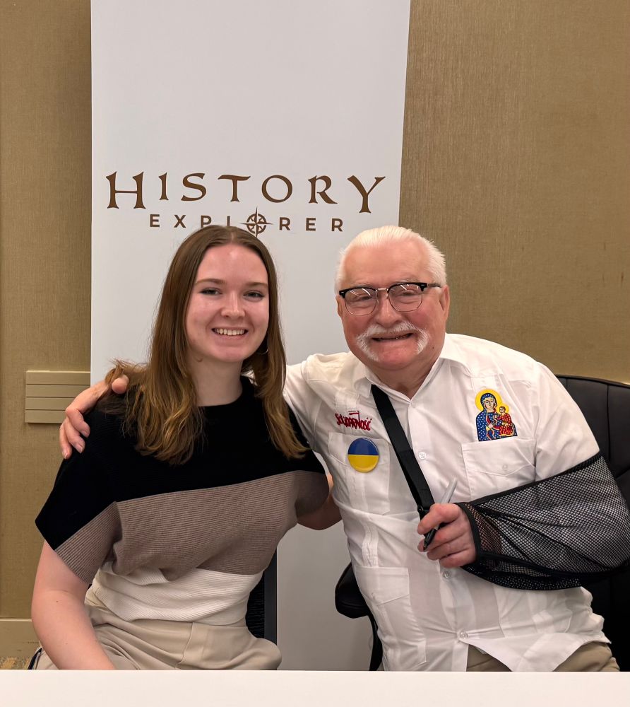 Lech Walensa seated, smiling with arm around young woman at a meet and greet