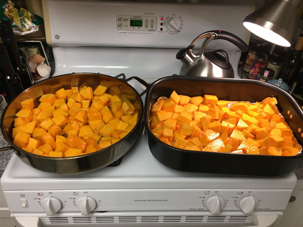 Two large pans of cut up orange squash sitting on a stove . 