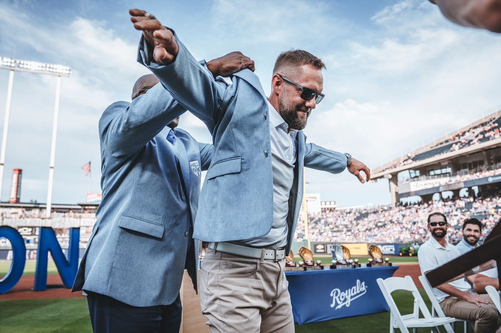 Bo Jackson lifts a powder blue Royals Hall of Fame jacket over Alex Gordon's shoulders.