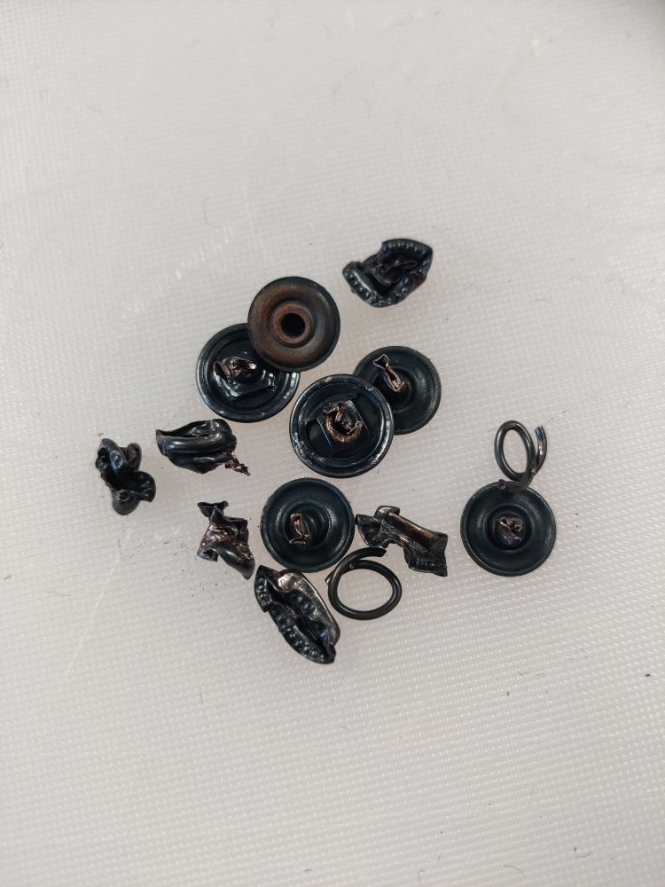 a tiny pile of mangled ex press studs. The rust is stark brown against the black plating. 