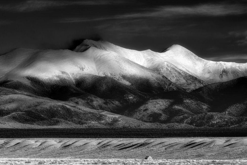 Sangre de Cristo Mountains


The Sangre de Cristo Mountains are one of the longest mountain ranges in the world covering a span of
250 miles, starting from Poncha Pass in Colorado to the lowest point Las Vegas, N.M. The highest
elevation within the range, is Blanca Peak at 14,345 feet, then Wheeler Peak at 13,161 feet, and Baldy
Peak, also known to the Tewa’s as “flower mountain,
” at 12,622 ft.

The ancestors of Pueblo Indians and the Apache, have lived within the mountains of the Sangres for
thousands of years. The mountain peaks are sources of spiritual energy, and sacred places of reverence
that encompass bodies of water which serve as doors to other realms. Rituals and prayers to these holy
entities kept a balance of harmony between man and nature.

Land was not revered in the same way by Spanish colonists. In many cases, Spanish colonists did not
individually own land; it was stewarded as a communal possession belonging to groups of settlers, or
clusters of villages. In 1719, the Spanish explorer Antonio Valverde y Cosio, reportedly was awestruck by
red-tinted snowy peaks at sunset, and called the mountain range, “Sangre de Cristo” or “Blood of
Christ.

” At the time, the Spanish referred to the mountains as the “Sierra Madre” or “Mother Mountain”
range.