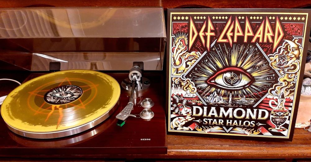 12” translucent yellow vinyl LP of Disc 1 of “Diamond Star Halos” by Def Leppard, on an ION turntable and side-by-side with the outer gatefold sleeve.