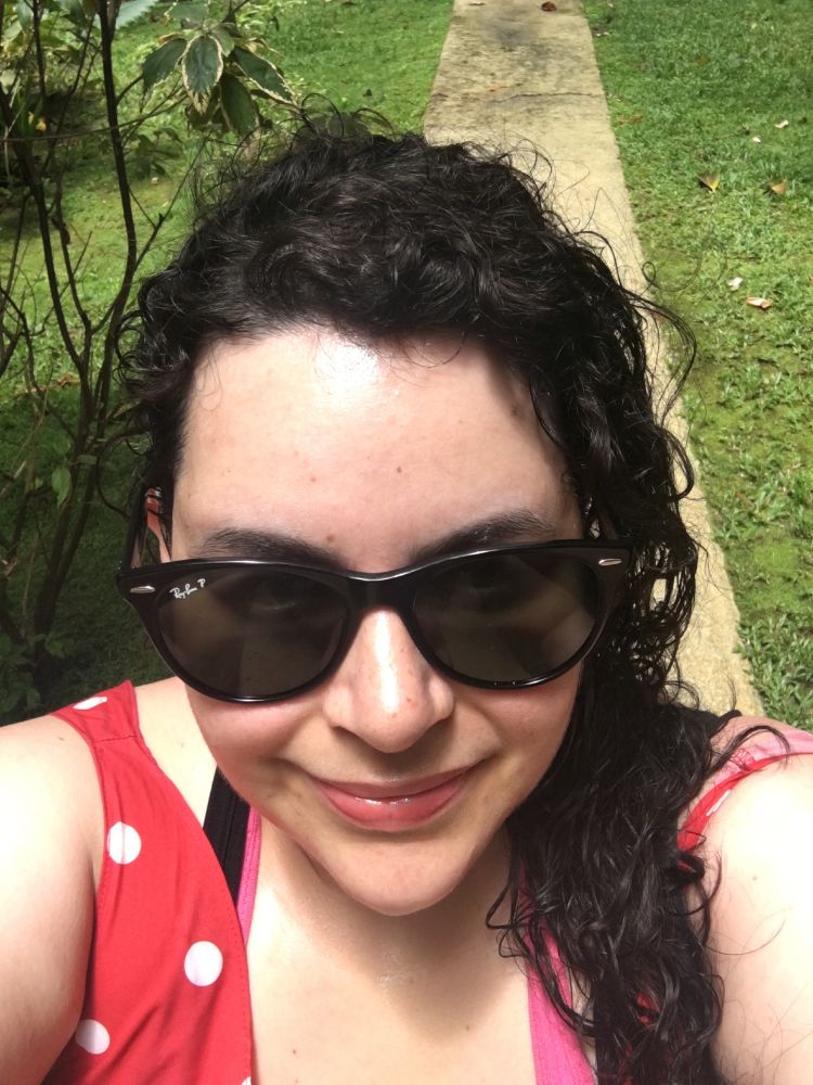 Photo of me, curly black hair in red dress with sunglasses, on a hill in Barbados. 