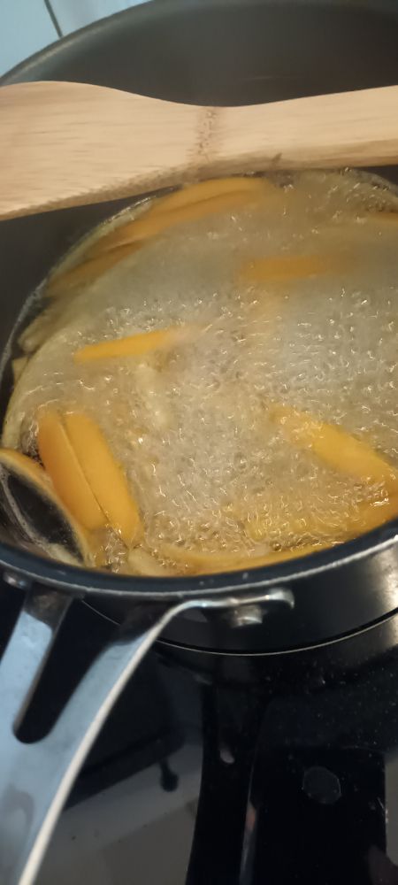Casserole avec de la peau d'orange coupées en lamelles, qui sont dans de l'eau sucrée qui bout