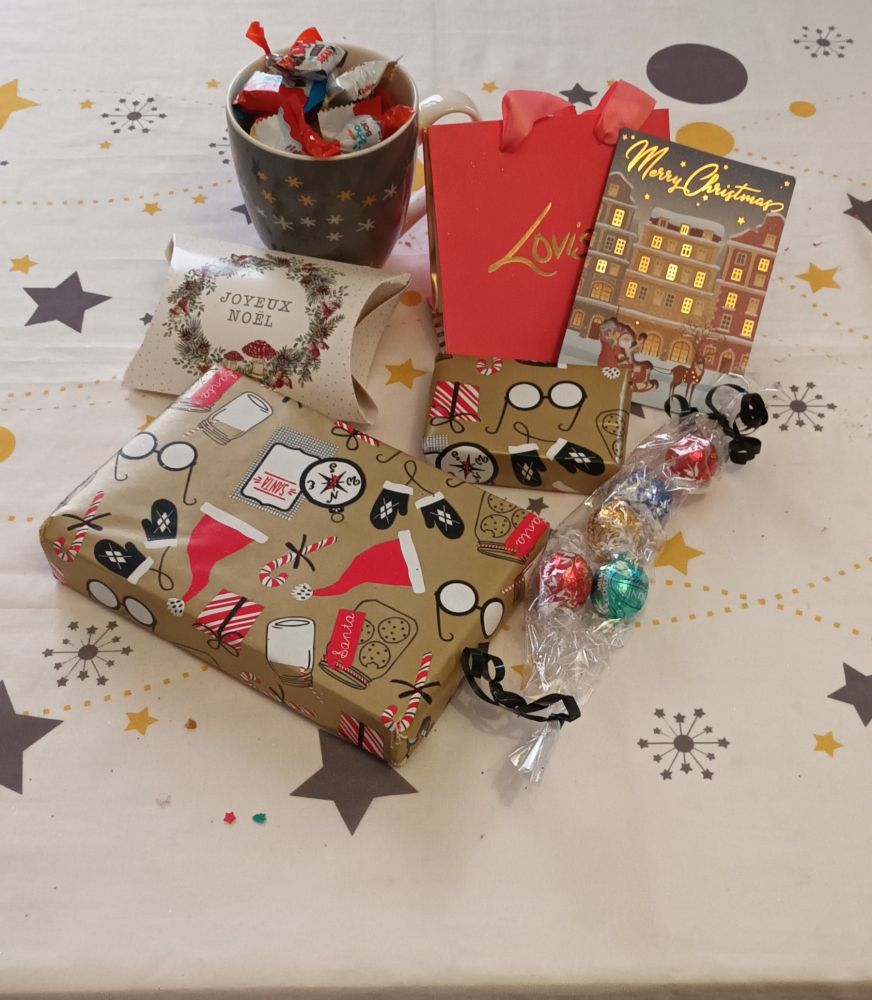 Une nappe avec plein de cadeaux empaquetés une carte de Noël et un mug rempli de chocolat de Noël 💝