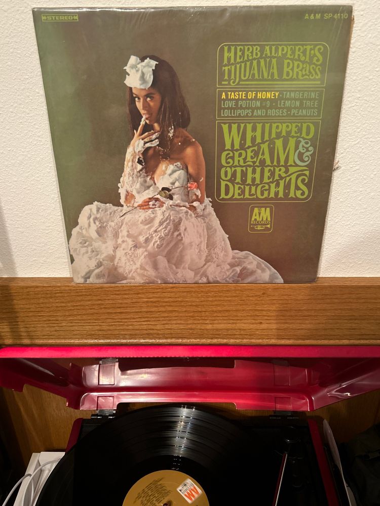 Album cover for Whipped Cream & Other Delights by Herb Alpert’s Tijuana Brass, showing a woman clothed only in whipped cream holding a pink rose
