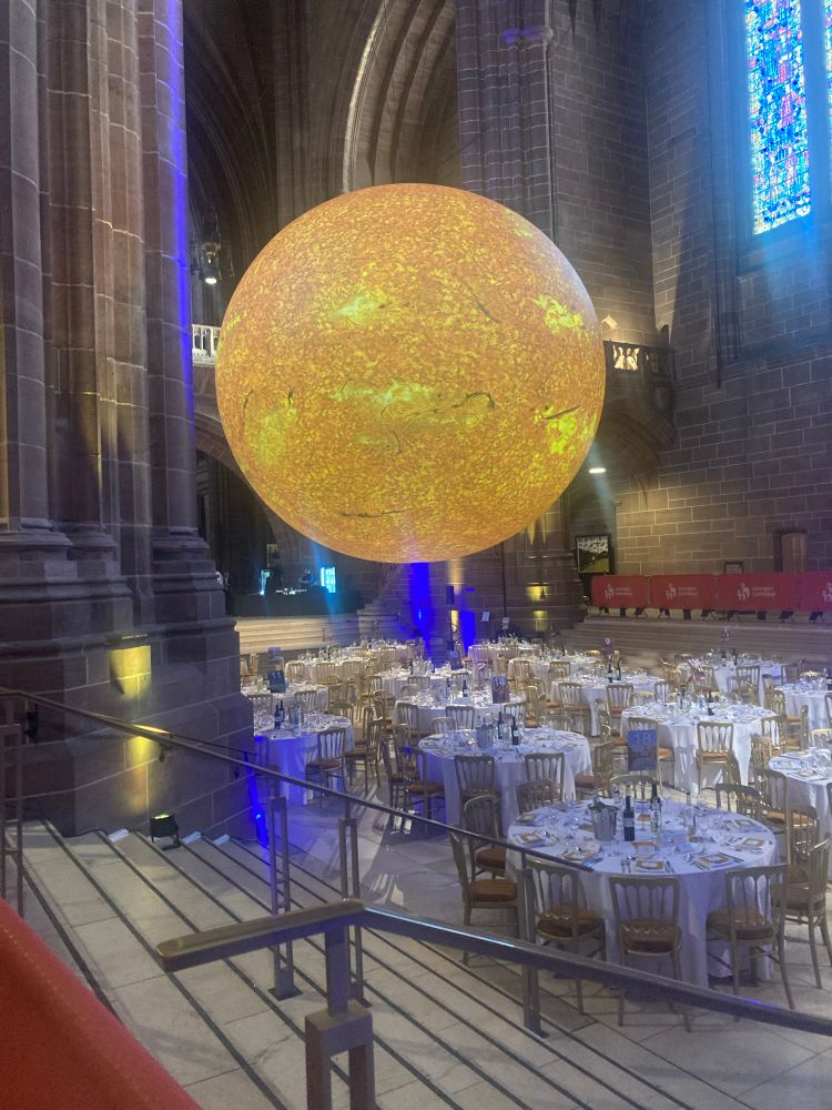 A picture of the sun dangling in the middle of cathedral which is set up for a formal dinner