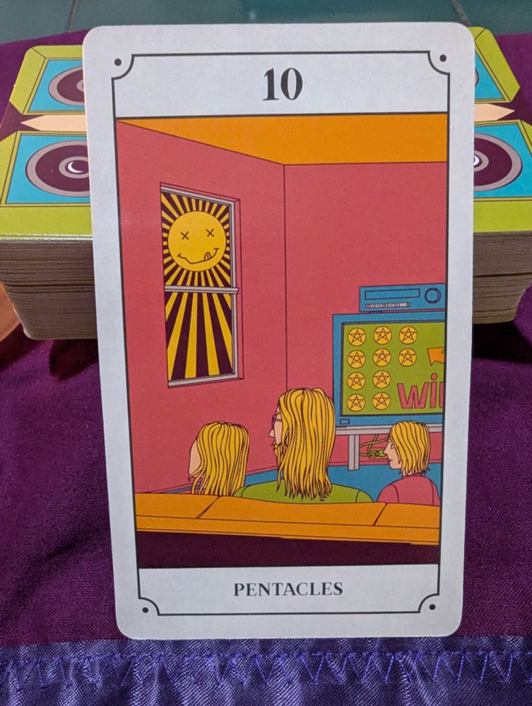 A close up shot of the 10 of Pentacles card from the Grunge Tarot deck. The card features a family sitting together on the sofa in their living room. They are surrounded by material comfort. They stare raptly out the window at a blazing sun.
