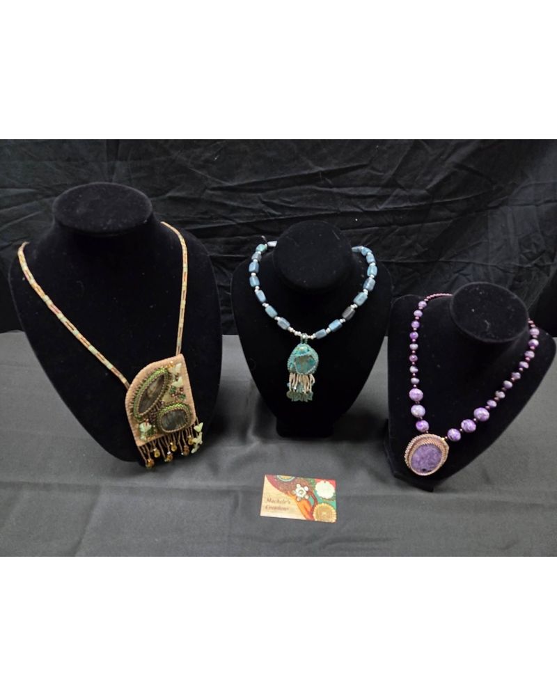 A picture of three necklaces. One is beaded embroidery with labradorite ($150 USD), and two are captured beadwork where the bezel is done with seed beads. The center one is dyed jasper (teal colored; $65 USD) and the right one is purple charoite ($75 USD) . 