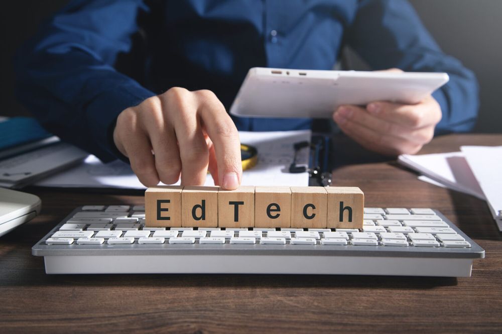 6 small cubes with each letter of edtech on a computer keyboard, with a man's finger placed on it. 
