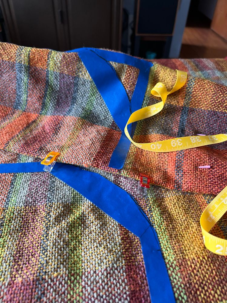 Handwoven plaid fabric with blue painters tape on it to mark where the seams of this shirt/jacket will end up. 