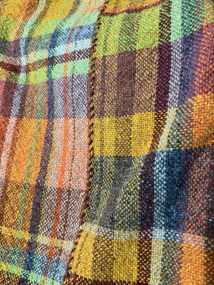 Handwoven plaid fabric with nine different colors and a hand stitched seam down the middle. 