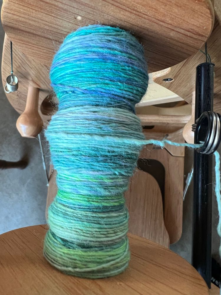 A spinning wheel with brightly colored wool yarn on it. 